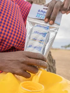 Person using Aquatabs water purification tablets to disinfect water in a portable container